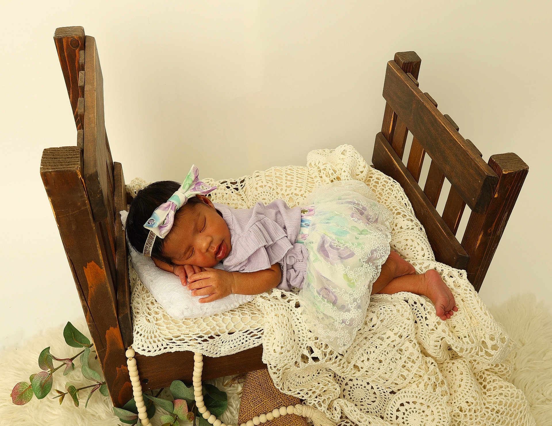 Daniella is registered to the contest to win money with this photo: newborn, baby, sleeping, wooden_bed, crochet_blanket, pastel_colors, headband, lace, pillow, cozy, nursery, soft_fabric, indoor, portrait, peaceful, cute, decor, greenery, beads, infant