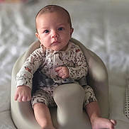 Presley is registered to the contest to win money with this photo: baby, infant, bumbo_seat, onesie, patterned_clothing, sitting, indoor, bed, blanket, soft_focus, cute, child, small_hands, small_feet, face, looking_at_camera, expression, comfort, home, young_child