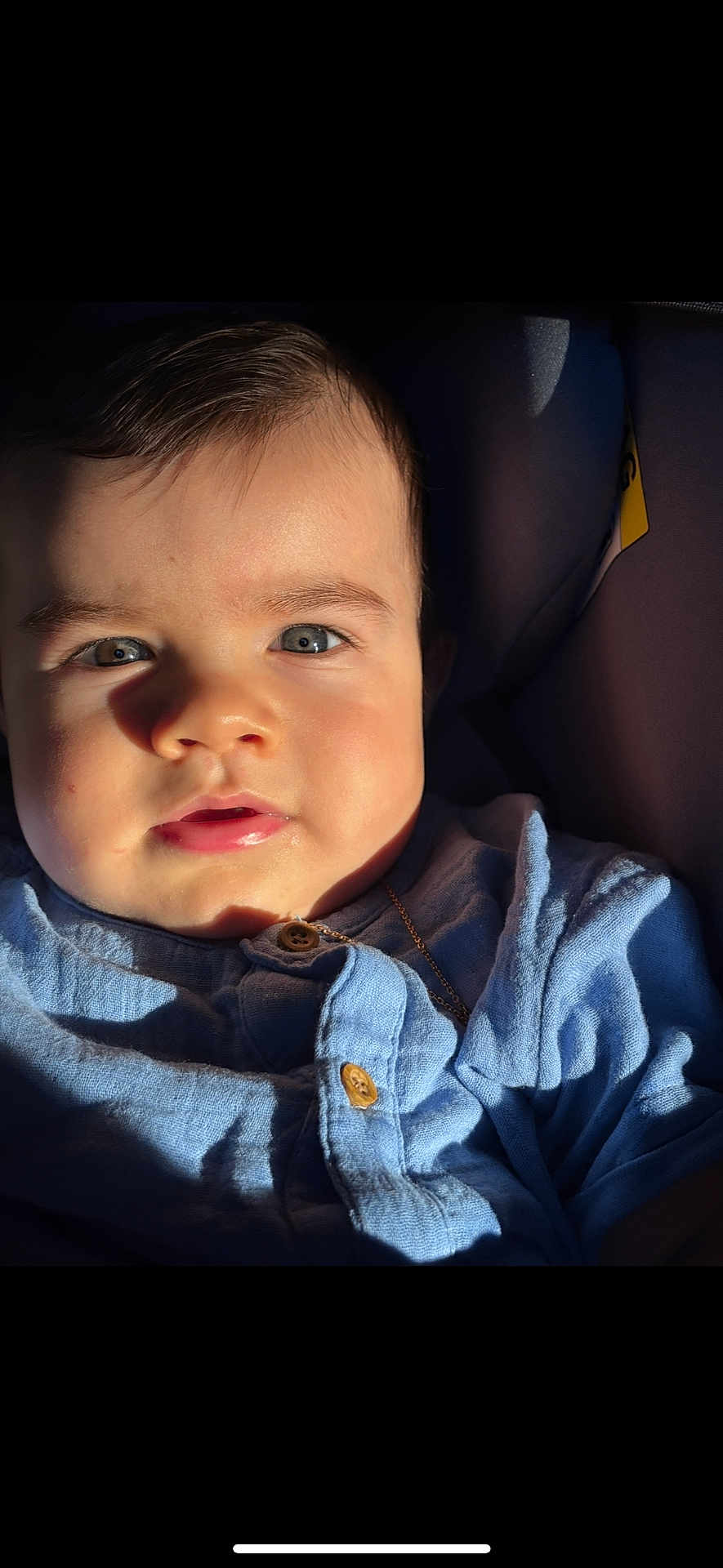 Rafaël a rejoint le concours — aidez-le/la à gagner de superbes lots ! baby, child, face, blue_eyes, blue_shirt, buttoned_shirt, close_up, portrait, sunlight, shadow, infant, young_child, skin, hair, expression, indoors, seat, clothing, person, cute