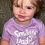 Elayna joined the competition — help win amazing prizes! toddler, child, smiling, purple_shirt, text_on_clothing, sitting, couch, indoor, portrait, face, hair, eyes, hands, cute, happy, casual_clothing, person, young_child, closeup, expression