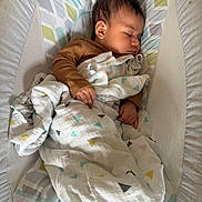 Jazer is registered to the contest to win money with this photo: baby, sleeping, blanket, brown_clothing, baby_lounger, patterned_fabric, infant, peaceful, cozy, cushion, indoors, child, resting, soft_light, cute, head, face, hand, portrait, comfort