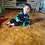 barefoot, black_clothing, cabinet, child, curious, cute, floor, furniture, home, indoor, person, portrait, sitting, smile, snack, teal_clothing, tile, toddler, toy, young_child
