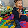 Maïlo participe au concours pour gagner de l'argent avec cette photo : toddler, child, baby, microphone, toy, playmat, foam_mat, colorful, pajamas, indoor, playpen, books, soft_toys, floor, curious, sitting, chewing, young_child, playtime, home