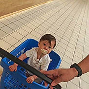 Maïlo participe au concours pour gagner de l'argent avec cette photo : toddler, child, laundry_basket, pacifier, shopping, store, floor_tiles, hand, white_shirt, indoor, person, grocery_store, curious, baby, walking, shopping_cart, blue, floor, casual, adult_hand