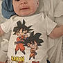 baby, infant, child, onesie, anime, cartoon, blanket, clothing, cute, face, portrait, soft, lying_down, hands, text, graphic_tshirt, brown_pants, indoor, relaxed, expression