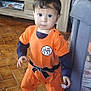 toddler, child, standing, orange_outfit, anime_costume, indoors, floor_tiles, barefoot, face, short_hair, playpen, furniture, cabinet, curious, young_child, person, home, portrait, looking_at_camera, cute