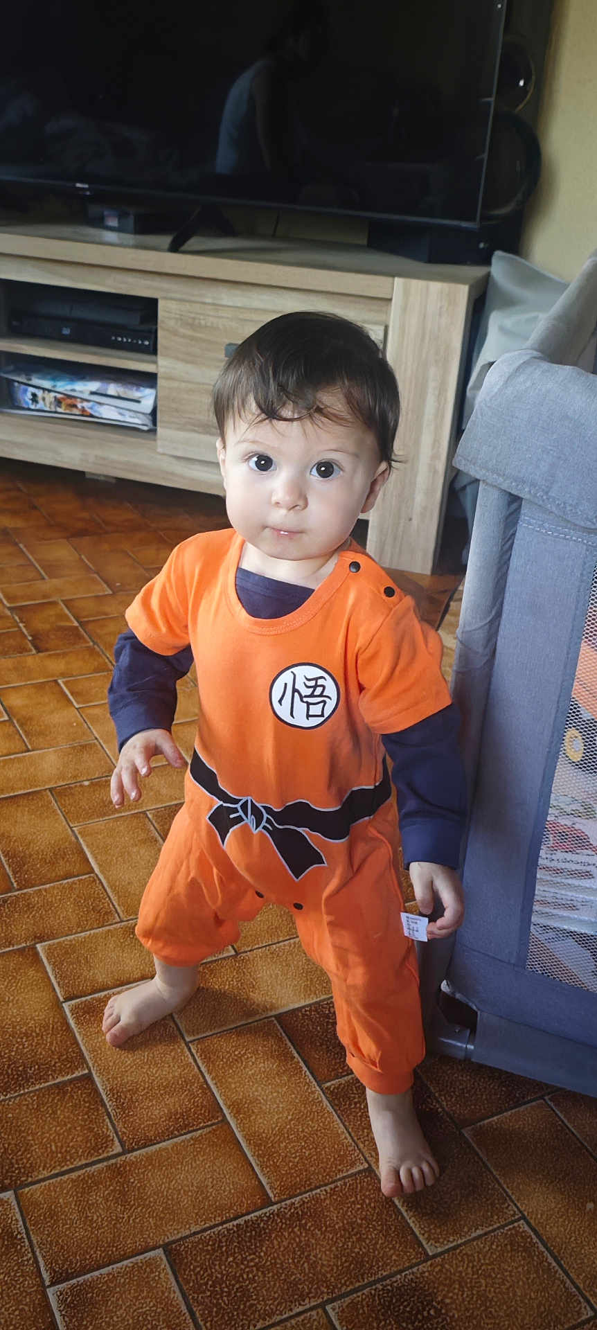 Maïlo joined the competition — help win amazing prizes! toddler, child, standing, orange_outfit, anime_costume, indoors, floor_tiles, barefoot, face, short_hair, playpen, furniture, cabinet, curious, young_child, person, home, portrait, looking_at_camera, cute