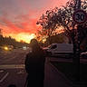 calm, car, clouds, dog, evening, footwear, leash, nature, outdoor, person, sidewalk, silhouette, sky, speed_limit_sign, street, sunset, traffic, trees, urban, van