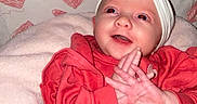 Clara joined the competition — help win amazing prizes! baby, infant, child, red_clothing, headband, bow, clapping_hands, smiling, happy, heart_pattern, blanket, indoors, cute, portrait, young_child, warm_clothing, pink_blanket, background_pattern, seated, playful