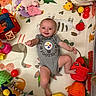 Clara joined the competition — help win amazing prizes! baby, infant, onesie, football, play_mat, toys, colorful, smiling, happy, child, indoor, soft_toys, plastic_balls, stuffed_animal, basket, play_area, crawling, cute, person, laying_down