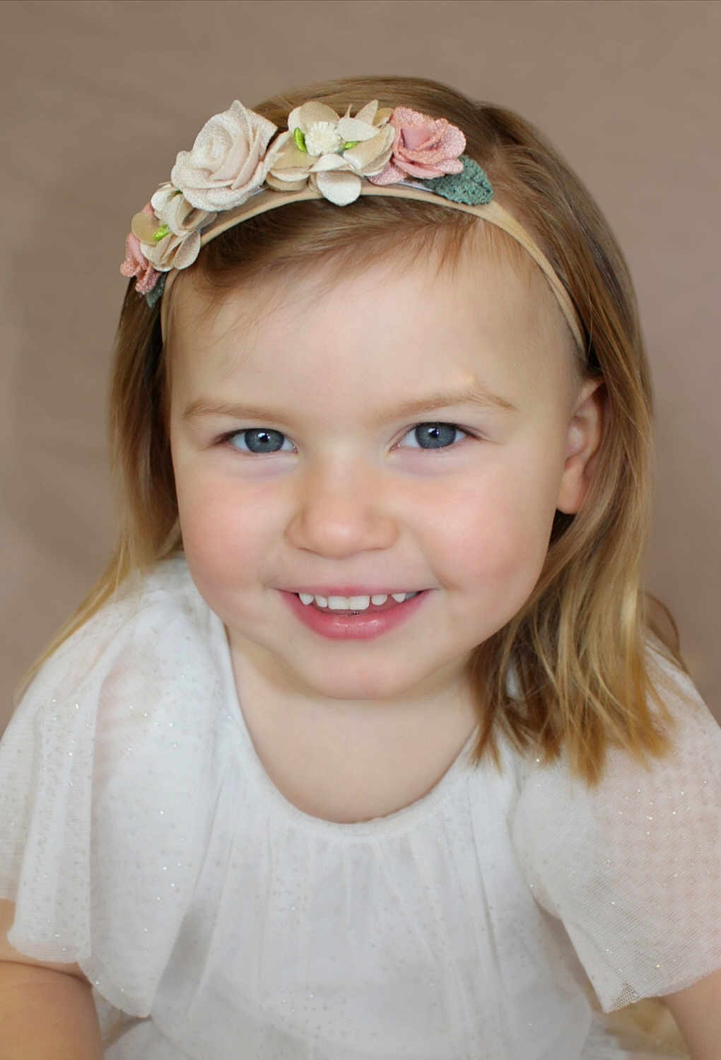 Margot a rejoint le concours — aidez-le/la à gagner de superbes lots ! child, toddler, girl, smiling, blue_eyes, headband, floral_headband, white_dress, portrait, face, happy, cute, young_child, blonde_hair, short_hair, indoor, soft_lighting, closeup, person, innocence