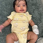 Aira joined the competition — help win amazing prizes! baby, infant, yellow_onesie, floral_pattern, white_mitten, pink_socks, lying_down, textured_surface, curly_hair, cute, child, portrait, indoors, soft_lighting, small_hands, small_feet, expression, face, skin, person