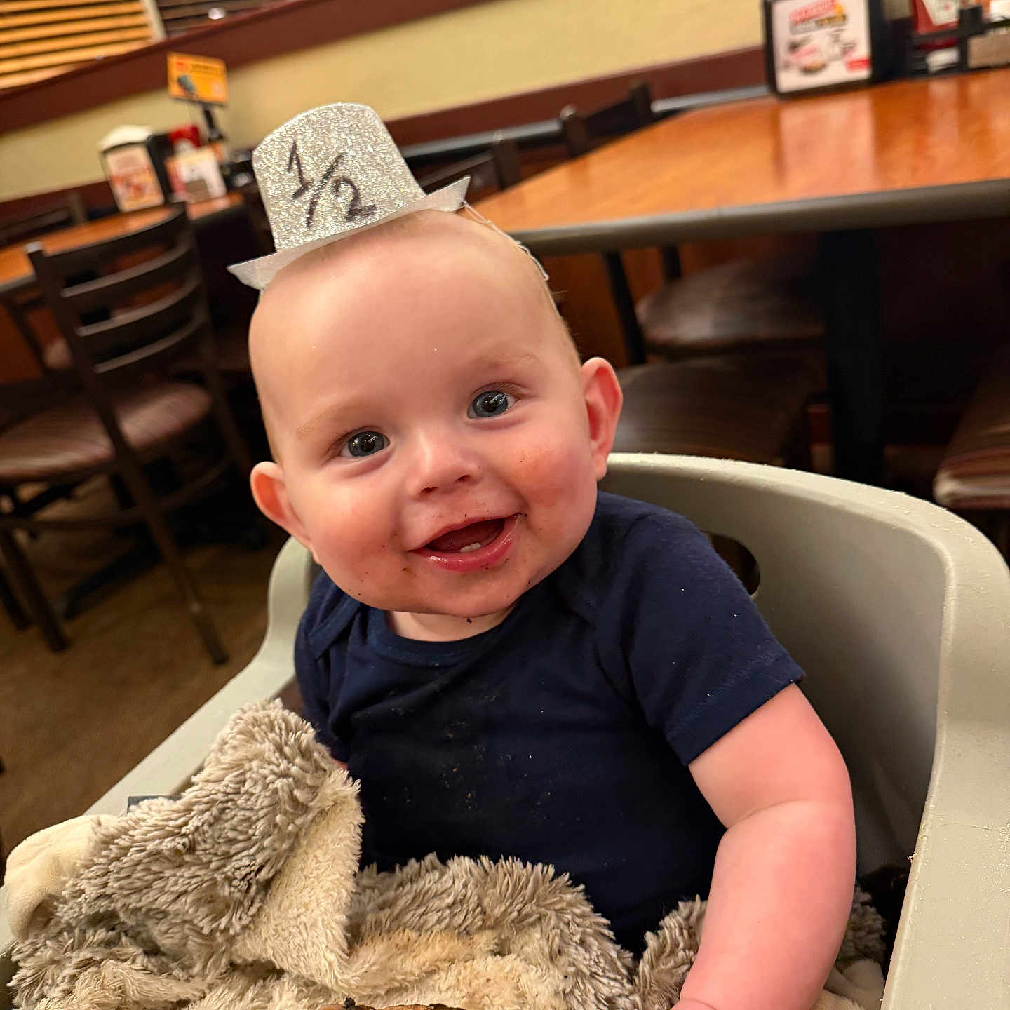 Waylon joined the competition — help win amazing prizes! baby, blanket, blue_shirt, chairs, cute, food, glitter_hat, half_birthday, half_hat, happy, highchair, indoor, infant, meat, messy_face, plush_blanket, portrait, restaurant, smiling, table