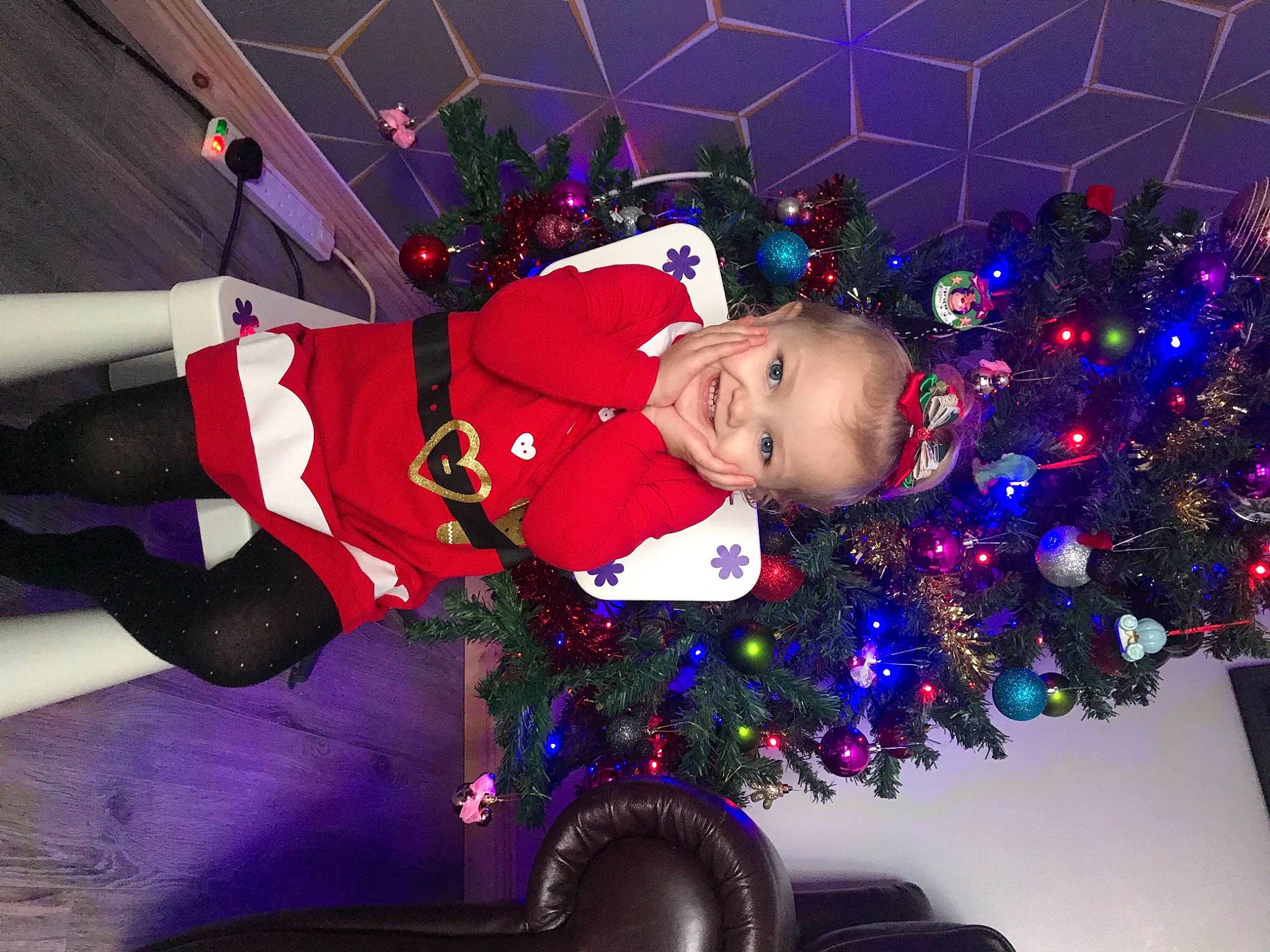 Lilly-rose is registered to the contest to win money with this photo: baby, carmine, christmas, christmas_decoration, christmas_eve, christmas_lights, christmas_ornament, christmas_tree, conifer, costume_accessory, event, fictional_character, holiday, holiday_ornament, interior_design, joy, ornament, person, pleased, red