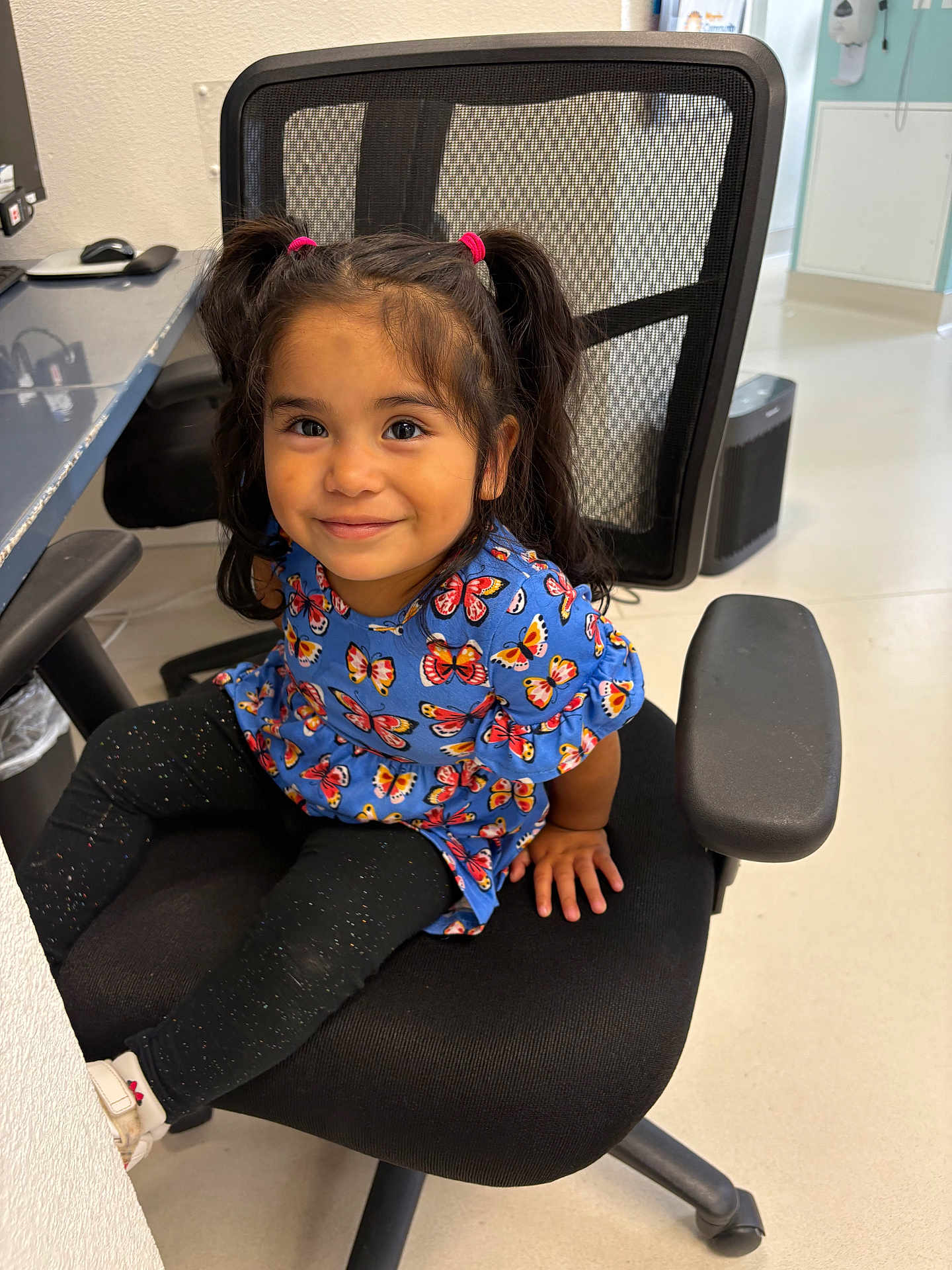 Sarai Lopez joined the competition — help win amazing prizes! child, girl, pigtails, smile, blue_dress, butterfly_pattern, black_chair, office_chair, indoor, floor, white_wall, black_leggings, white_shoes, happy, portrait, person, furniture, cute, seated, young