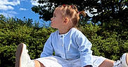 Angelina participe au concours pour gagner de l'argent avec cette photo : child, toddler, outdoor, blue_sky, clouds, greenery, tree, pigtails, white_shoes, white_pants, blue_top, sitting, curious, sunny_day, nature, grass, young_child, portrait, casual_clothing, playful