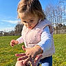 Angelina a rejoint le concours — aidez-le/la à gagner de superbes lots ! child, toddler, outdoor, grass, blue_sky, trees, pink_vest, blue_pants, hand, flowers, curious, nature, sunny, daylight, person, young_child, playing, field, season_winter, casual_clothing