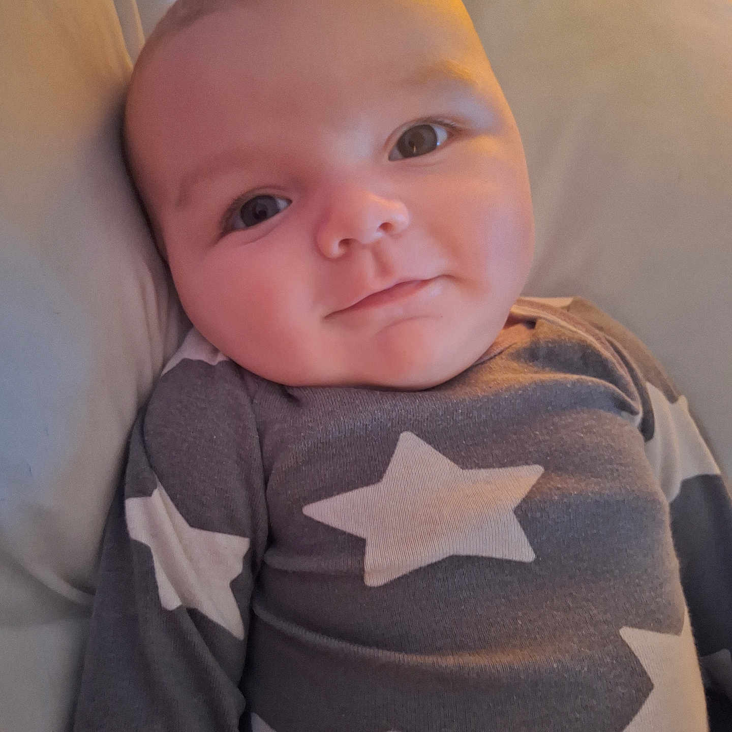 Jaxson is registered to the contest to win money with this photo: baby, cheeks, child, clothing, cute, expression, eyes, face, head, indoors, infant, lying_down, pajamas, portrait, skin, smile, soft_surface, star_pattern, warm_light, young