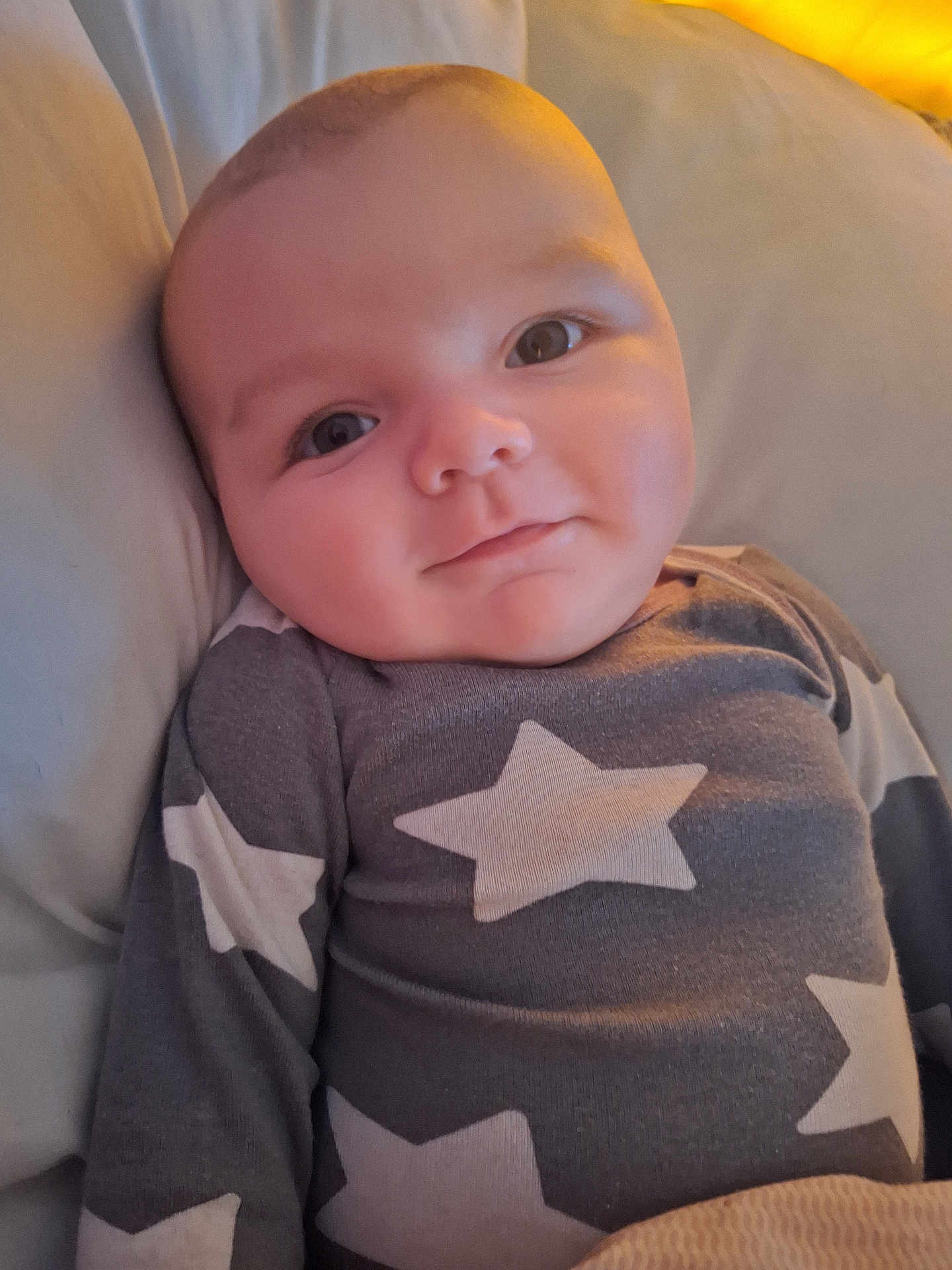 Jaxson is registered to the contest to win money with this photo: baby, child, face, smile, eyes, clothing, star_pattern, pajamas, infant, cute, lying_down, soft_surface, warm_light, portrait, indoors, head, skin, cheeks, young, expression