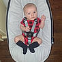 baby, infant, onesie, red_clothing, black_socks, baby_seat, safety_harness, wood_floor, indoor, person, cute, looking_at_camera, wide_eyes, small_hands, footwear, plush_seat, child, home, flooring, casual