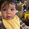 David Orro is registered to the contest to win money with this photo: baby, child, infant, face, bib, plaid_clothing, indoor, christmas_tree, holiday_decor, furniture, couch, curly_hair, curious_expression, person, portrait, hand, yellow_bib, home, cozy, seasonal