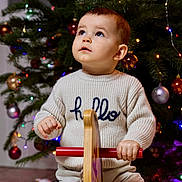 Mélio a rejoint le concours — aidez-le/la à gagner de superbes lots ! toddler, child, sweater, hello, rocking_horse, toy, christmas_tree, ornaments, lights, holiday, indoor, curious, gazing, festive, decorations, seated, play, winter_clothing, cute, young_child