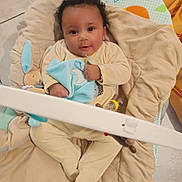 William participe au concours pour gagner de l'argent avec cette photo : baby, infant, onesie, toy, blanket, baby_seat, floor, curly_hair, cute, smiling, indoor, soft_toy, blue, cream, cushion, child, person, comfort, playtime, small