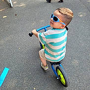 Souleyman participe au concours pour gagner de l'argent avec cette photo : child, boy, sunglasses, balance_bike, blue, striped_shirt, shorts, outdoor, pavement, footwear, people, walking, sunny, smile, casual_clothing, summer, play, toy, fun, park