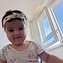 Amina a rejoint le concours — aidez-le/la à gagner de superbes lots ! toddler, child, headband, indoor, window, daylight, smile, face, person, clothing, short_sleeve, cherry_pattern, white_shirt, baby, cute, young_child, portrait, blurry, happy, casual
