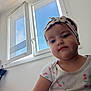 Amina a rejoint le concours — aidez-le/la à gagner de superbes lots ! toddler, child, indoor, window, headband, shirt, cherry_pattern, face, person, portrait, blue_sky, light, curious, expression, casual_clothing, young_child, natural_light, white_wall, home, seated