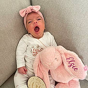 Elsie is registered to the contest to win money with this photo: baby, infant, yawning, pajamas, headband, bow, stuffed_animal, bunny, pink, plush_toy, wooden_sign, one_month, couch, beige, cozy, cute, child, portrait, indoor, soft