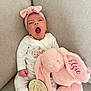 baby, infant, yawning, pajamas, headband, bow, stuffed_animal, bunny, pink, plush_toy, wooden_sign, one_month, couch, beige, cozy, cute, child, portrait, indoor, soft