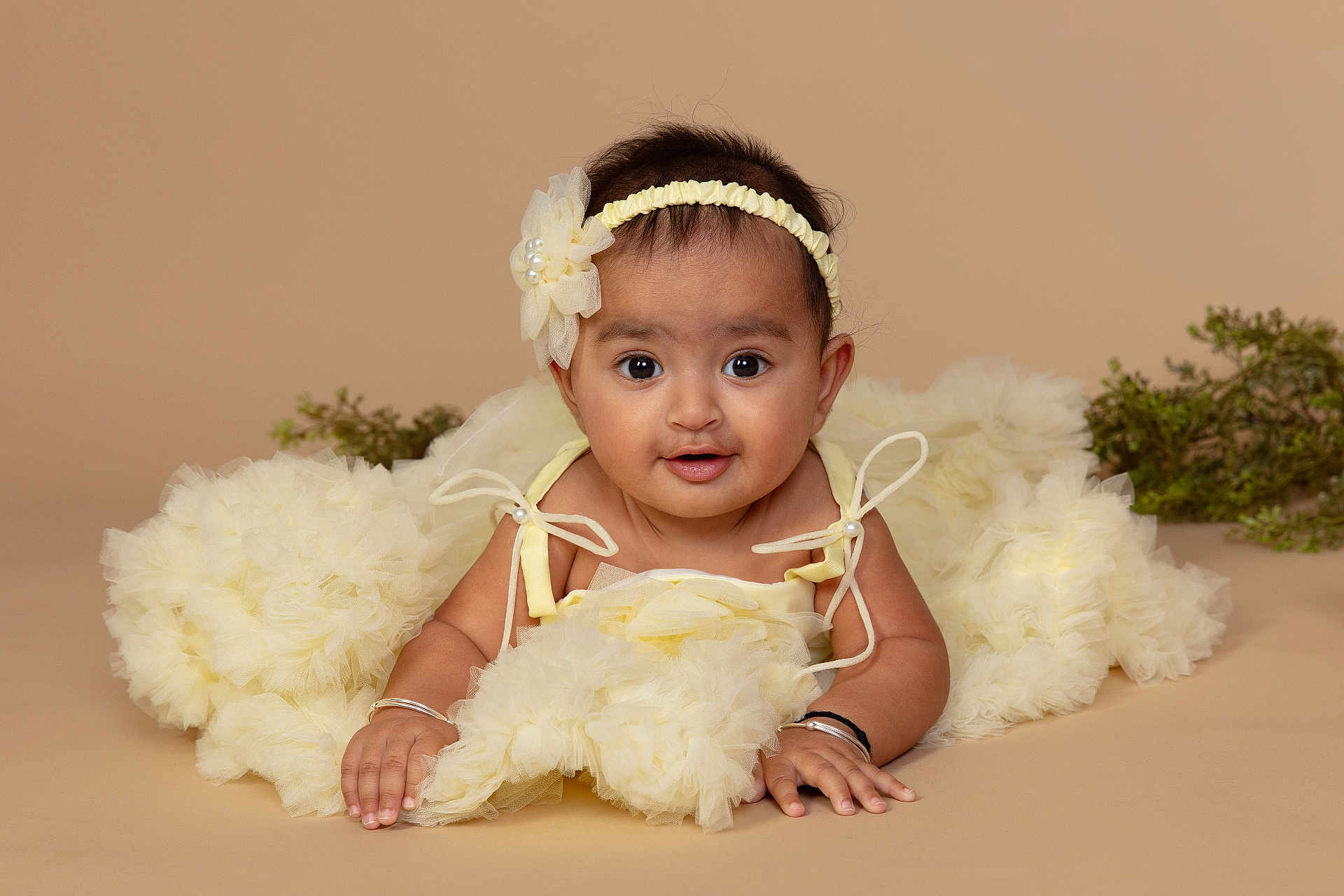 Vedaa is registered to the contest to win money with this photo: baby, bracelet, child, clothing, cute, dress, face, flower, greenery, hands, headband, indoors, infant, lying_down, portrait, skin, smiling, soft_background, studio, toddler
