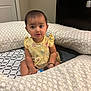 toddler, child, baby, yellow_dress, butterfly_pattern, bracelet, earrings, cushion, bed, indoor, person, furniture, floor, looking, sitting, cute, curious, young_child, home, expression