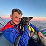 man, dog, boat, water, sunset, life_jacket, outdoor, smile, pet, animal, nature, sea, sky, happiness, friendship, travel, adventure, leisure, portrait, casual