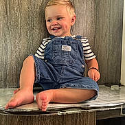 Tchad a rejoint le concours — aidez-le/la à gagner de superbes lots ! toddler, child, smile, barefoot, denim_overalls, striped_shirt, happy, dimples, sitting, wood_wall, indoor, cute, young_child, skin, portrait, foot, hand, clothing, person, casual