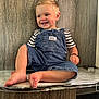 toddler, child, smile, barefoot, denim_overalls, striped_shirt, happy, dimples, sitting, wood_wall, indoor, cute, young_child, skin, portrait, foot, hand, clothing, person, casual