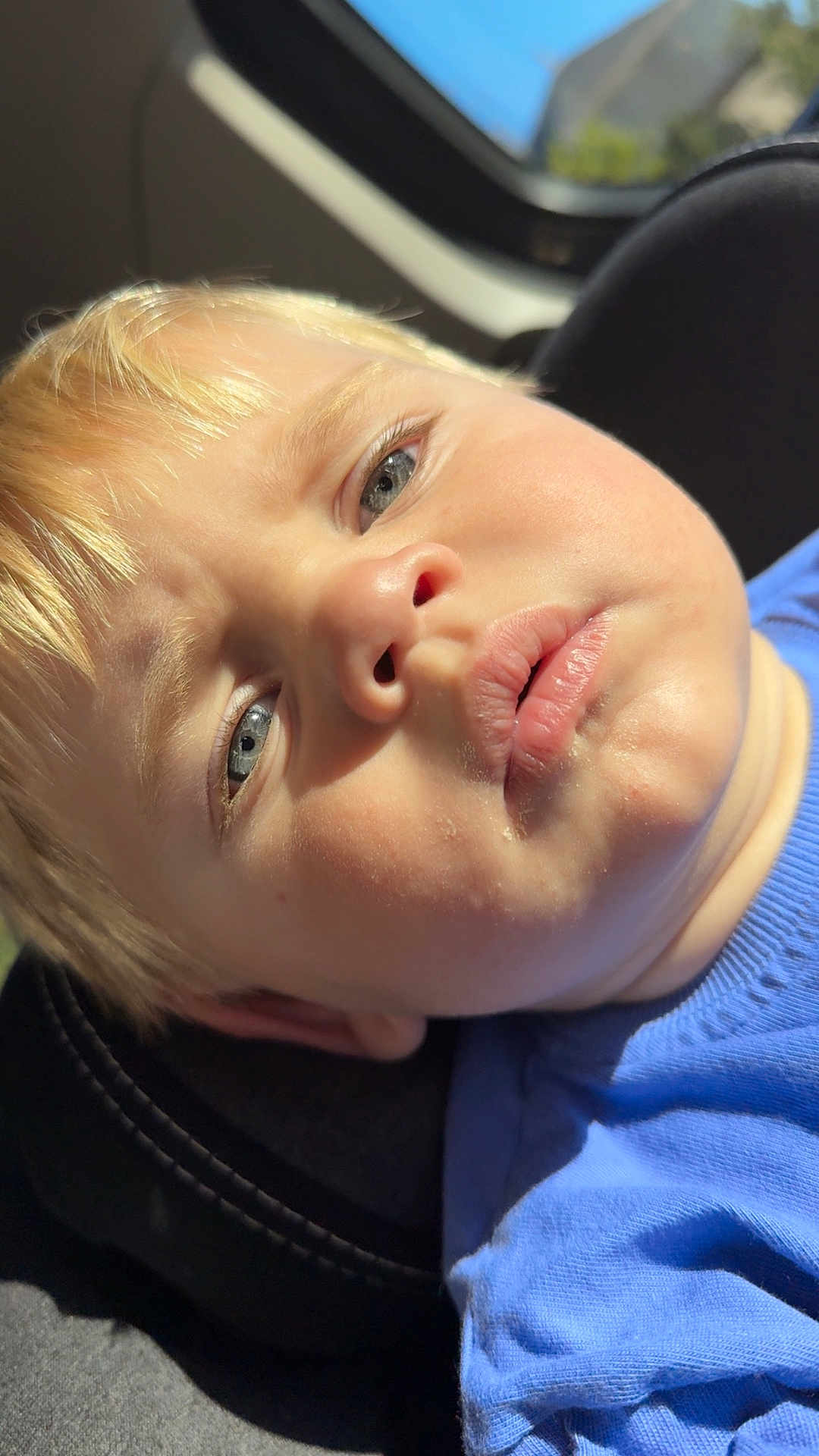 Tchad participe au concours pour gagner de l'argent avec cette photo : child, toddler, face, blue_shirt, car_seat, blonde_hair, close_up, portrait, sunlight, shadow, skin, eyes, lips, casual_clothing, indoors, seat, person, baby, head, young