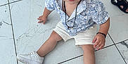 Tchad participe au concours pour gagner de l'argent avec cette photo : toddler, child, sitting, floor, marble_floor, white_shoes, blonde_hair, blue_eyes, shorts, shirt, curious_expression, indoor, footwear, person, cute, casual_clothing, young_child, looking_up, necklace, bracelet