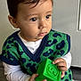 toddler, child, toy, block, green, vest, sitting, indoor, curious, brown_eyes, knitwear, long_sleeve_shirt, pants, floor, wooden_floor, portrait, young_child, cute, casual_clothing, closeup
