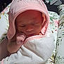 newborn, baby, blanket, pink_hood, sleeping, face, hand, cushion, floral_pattern, soft_lighting, indoors, wrapped, peaceful, cute, child, portrait, infant, resting, fabric, cozy