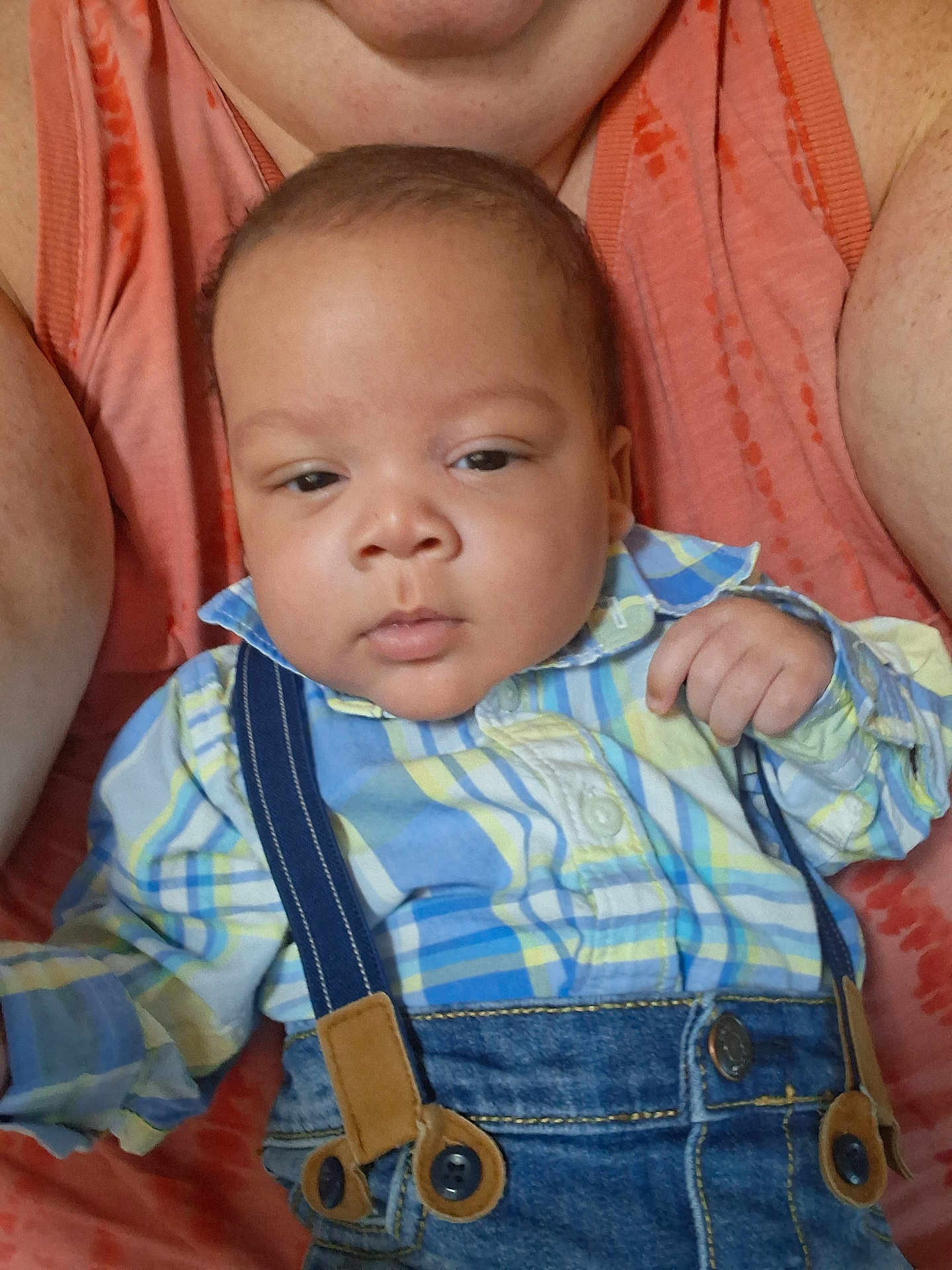Adriel is registered to the contest to win money with this photo: baby, infant, child, person, face, clothing, shirt, denim, suspenders, plaid, adult, arm, skin, casual_wear, portrait, indoor, closeup, expressionless, holding, cute
