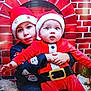 Axel a rejoint le concours — aidez-le/la à gagner de superbes lots ! child, baby, santa_hat, christmas_outfit, holiday, festive, red_clothing, brick_wall, fireplace, smiling, cute, indoor, portrait, holding, toddler, sweater, face, people, celebration, seasonal