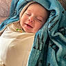 baby, blanket, blue_blanket, couch, face, happy, infant, indoors, laying_down, patterned_blanket, peaceful, portrait, resting, sleeping, soft_texture, smile, toddler, wrapped, young_child, cozy