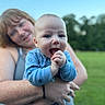 Wes joined the competition — help win amazing prizes! baby, adult, blue_onesie, smiling, happy, outdoor, greenery, grass, trees, daylight, holding, person, portrait, nature, tattoo, hand, skin, head, face, background_blur