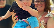 Wes is registered to the contest to win money with this photo: baby, child, woman, person, outdoor, glasses, tree, hand, face, blue_pants, black_shirt, holding, smile, nature, family, adult, blurry_background, casual_clothing, watch, portrait