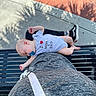 Wes is registered to the contest to win money with this photo: baby, pacifier, onesie, bench, outdoor, sidewalk, shadow, person, lap, sneakers, tattoo, relaxing, nap, child, gray_clothing, black_bench, sunlight, palm_shadow, casual, footwear