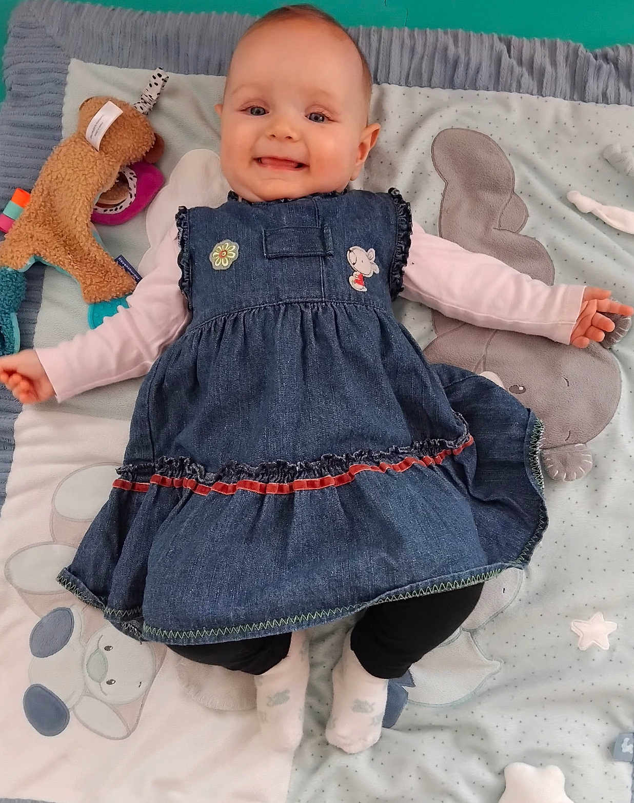 Jolyne a rejoint le concours — aidez-le/la à gagner de superbes lots ! baby, infant, smiling_baby, denim_dress, long_sleeve, socks, toy, stuffed_animal, play_mat, blanket, pillow, hand, legs, face, eyes, mouth, cheek, cute, indoor, lying_down