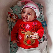 Jolyne a rejoint le concours — aidez-le/la à gagner de superbes lots ! baby, infant, smiling, christmas_sweater, reindeer, red_clothing, pink_hat, holiday, toy, teething_ring, pacifier, crib, blanket, patterned_sheet, playmat, cute, happy, portrait, lying_down, child