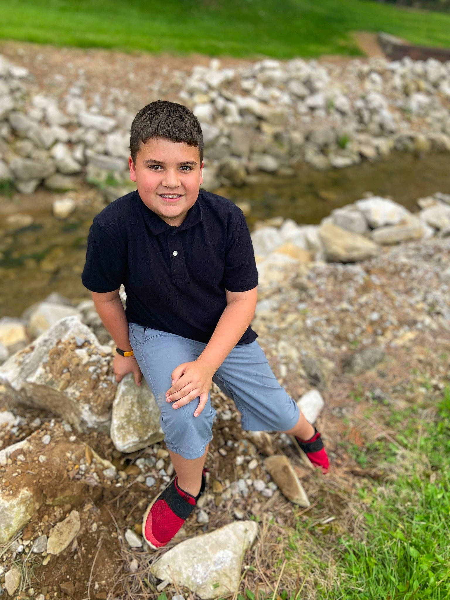 Gavin is registered to the contest to win money with this photo: bedrock, child, fun, grass, happy, joy, landscape, leisure, outcrop, people_in_nature, person, recreation, rock, shorts, sitting, smile, soil, spring, t_shirt, thigh